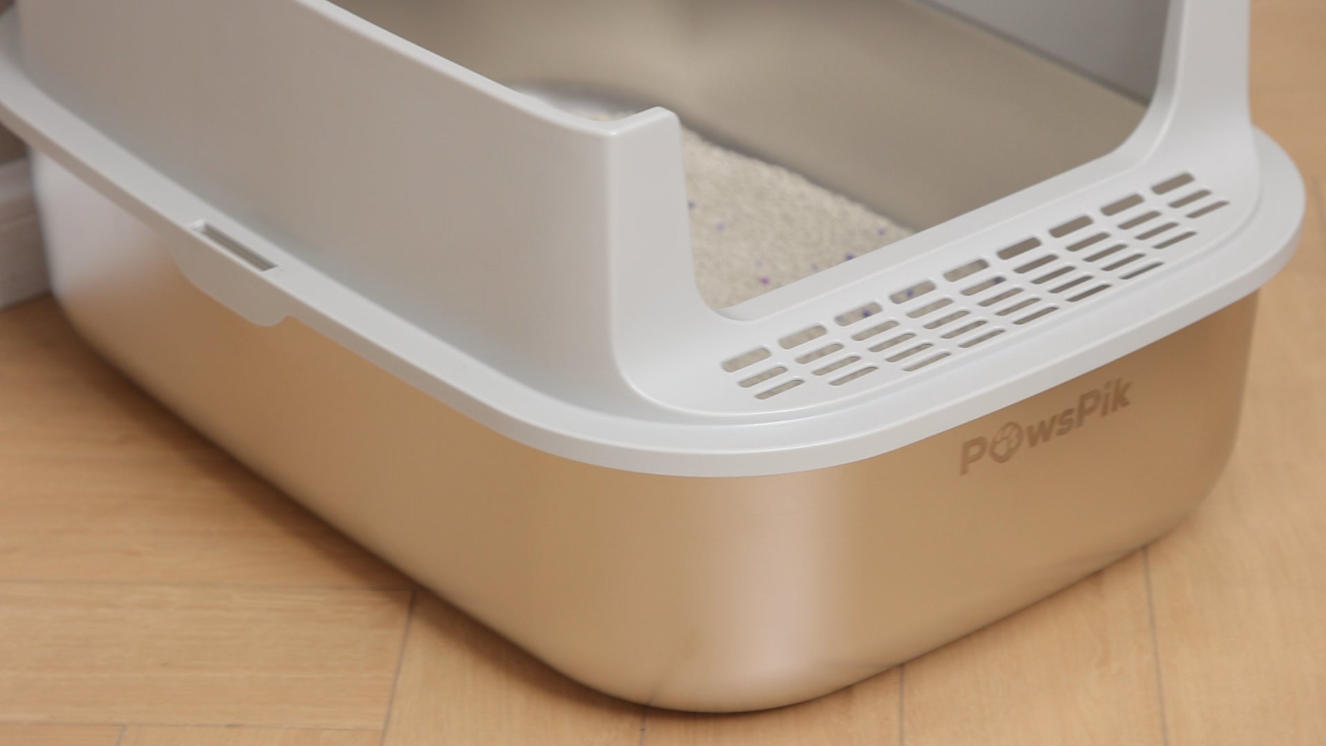 An open cat litter box by PawsPik with a beige base featuring “round corners” and white rim on a wooden floor.