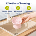Load image into Gallery viewer, A hand holding a pink, cat-shaped slow feeder bowl drips water above a sink, highlighting its smooth surface and dishwasher-safe features.