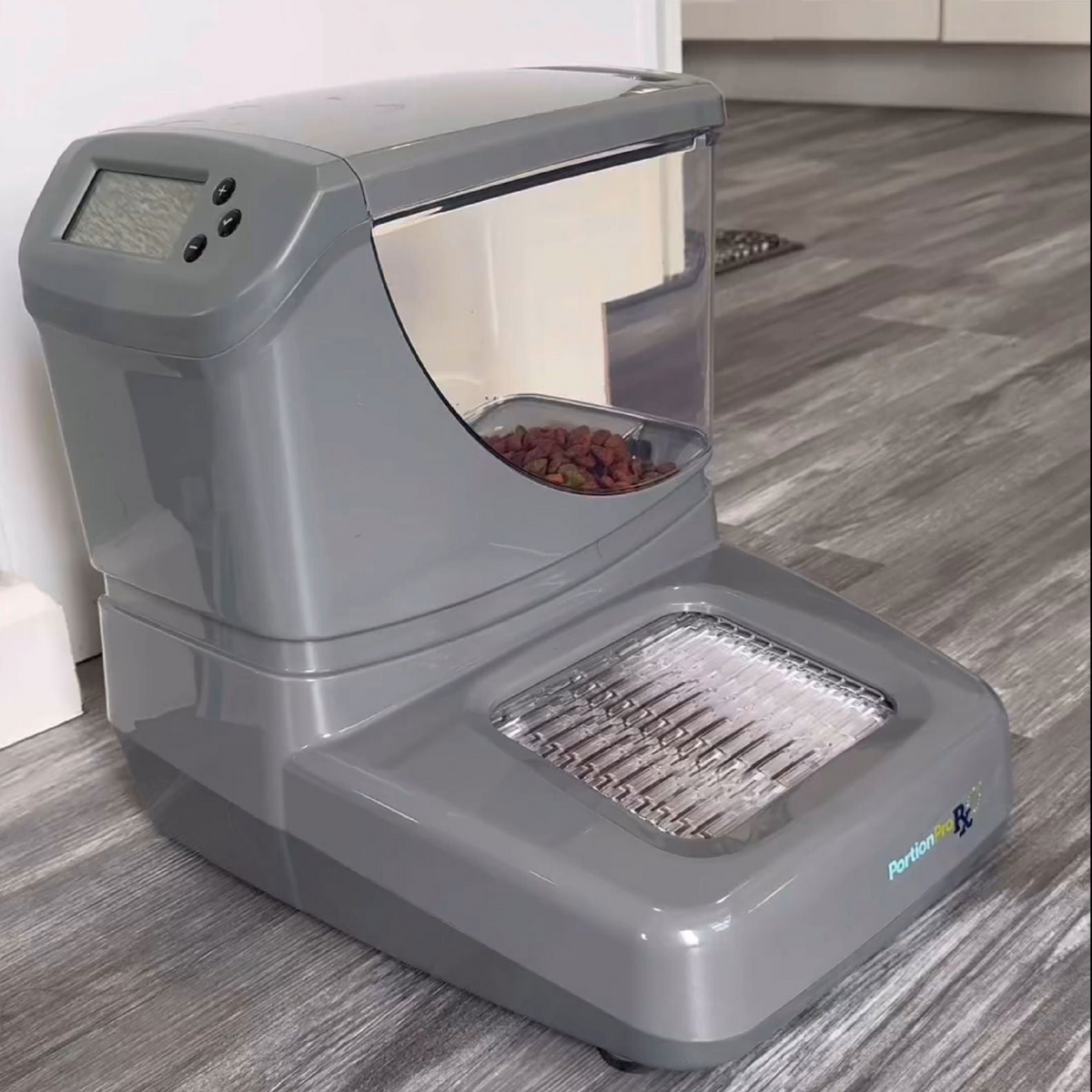 PawsPik Automatic pet feeder with digital display and filled food compartment on a wood floor.