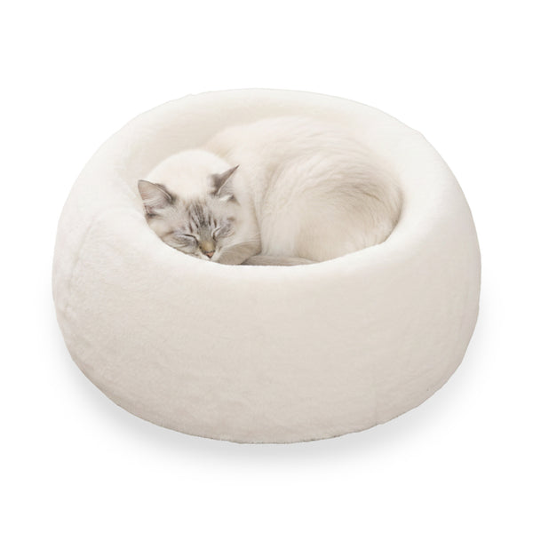 A fluffy white cat is peacefully curled up asleep in a cozy, white round cat bed.