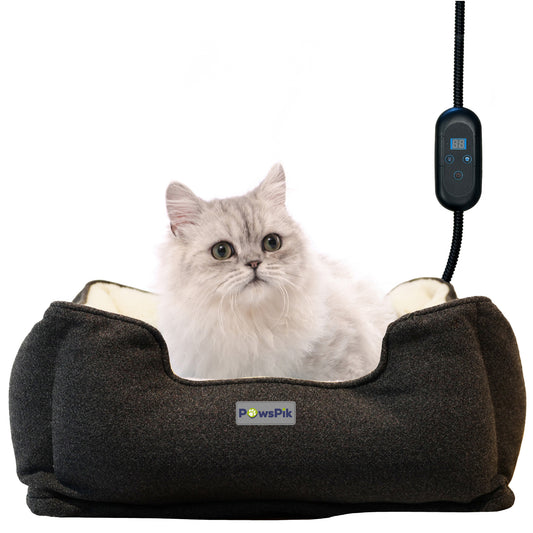 A fluffy gray and white cat sitting in a charcoal colored PawsPik heated cat bed, with a hanging pet bed warmer controller.