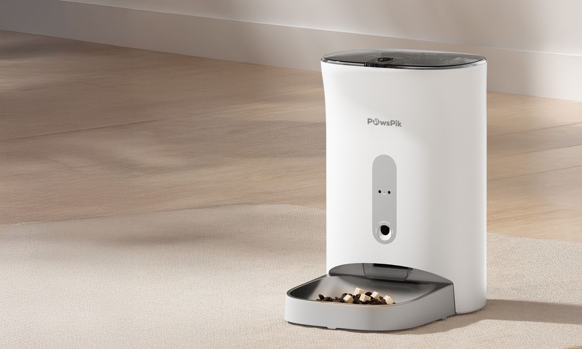A sleek white automatic cat feeder dispenses kibble into a gray dish on a light carpeted floor, angled in soft natural light, creating a calm atmosphere.