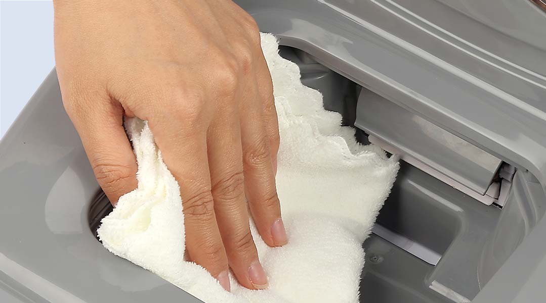 A hand cleaning gray pet food dispenser with a white towel.